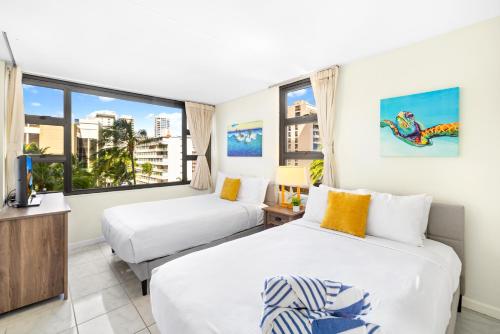 two beds in a room with a window at Waikiki Banyan Oasis with Partial Ocean View, 1-Block to Beach, Free Parking in Honolulu
