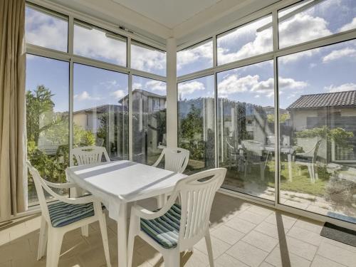 une table et des chaises blanches dans une chambre avec fenêtres dans l'établissement Villa 2 chambres proche plage, jardin, véranda, clim, wifi à Biscarrosse - FR-1-521-19, à Biscarrosse-Plage