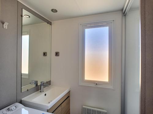 een witte badkamer met een wastafel en een spiegel bij Mobil-Home Jullouville, 4 pièces, 6 personnes - FR-1-361A-9 in Jullouville-les-Pins