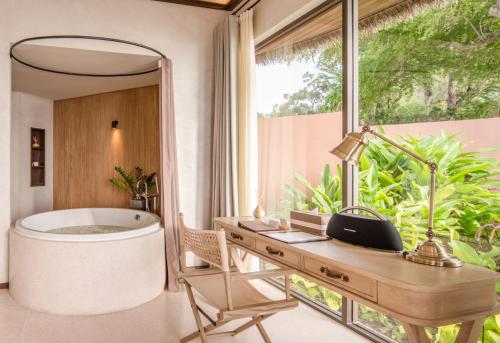a bathroom with a tub and a desk and a mirror at VALA Hua Hin - Nu Chapter Hotels in Cha Am