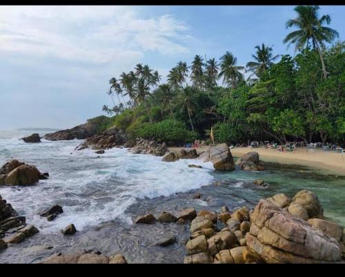 a beach with rocks and palm trees and the ocean at Pravindi Guest Home in Mirissa