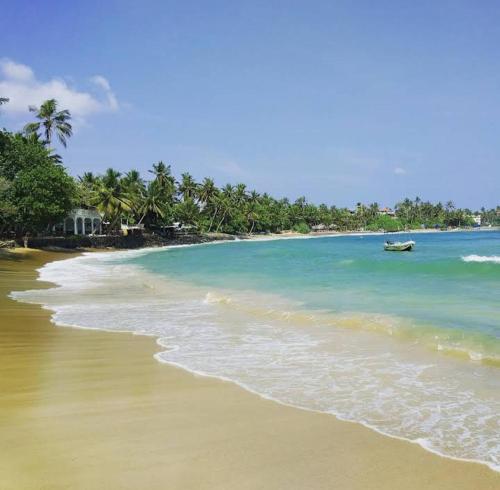 a beach with a boat in the water at Pravindi Guest Home in Mirissa