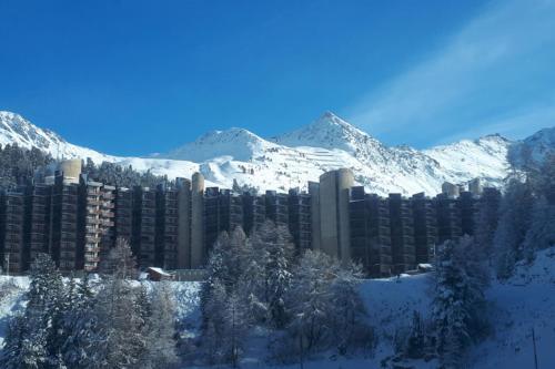 duży budynek z pokrytymi śniegiem górami w tle w obiekcie Studio Near The Slopes At La Plagne w mieście La Plagne Tarentaise