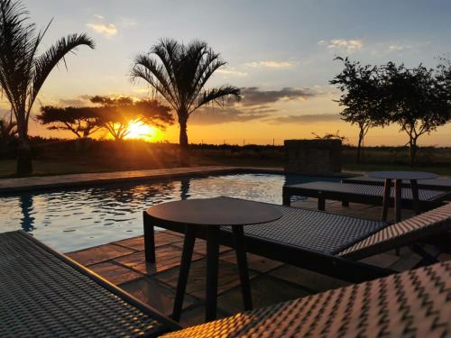 a pool with two tables and a sunset in the background at Blackwood Eco Lodge in Witbank