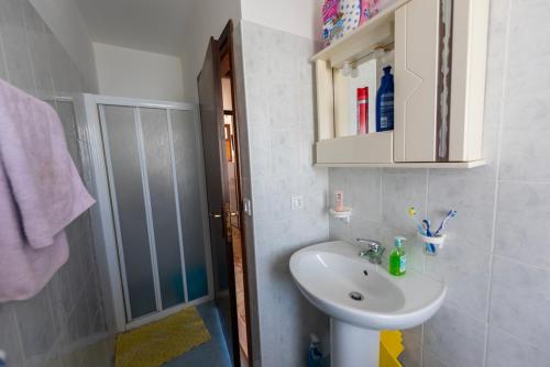 La salle de bains blanche est pourvue d'un lavabo et d'une douche. dans l'établissement Condominio Carina Sud, à Bibione