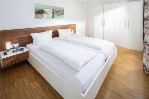 een groot wit bed in een kamer met een houten vloer bij Schippers Huus 03 - Bremen in Norderney