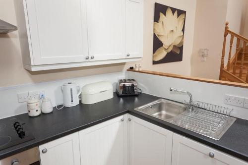 a kitchen with white cabinets and a sink and a counter at Appletree Cottage at Williamscraig Holiday Cottages in Linlithgow