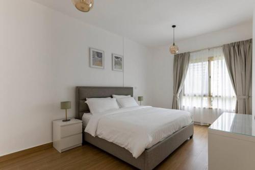 a white bedroom with a bed and a window at Bright & Relaxing 1BR Apartment in Dubai