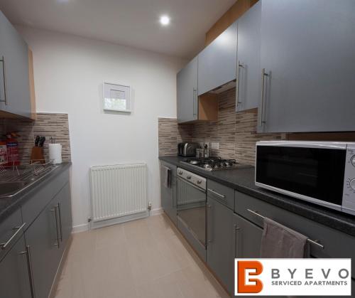 a kitchen with gray cabinets and a microwave at ByEvo 6 Brabloch - Close to GLA - Perfect Getaway or Working away from Home in Paisley