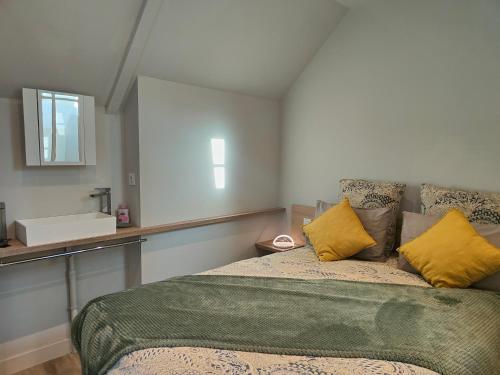 1 dormitorio con cama con almohadas amarillas y lavamanos en La petite maison, en Dinan