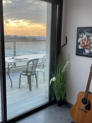 Habitación con balcón con mesa y guitarra. en פנטהוז ונוף עוצר נשימה, שקט אפשרות בקומה העליונה לחדר משרד הפנטהוז מיועד לאורחים, en Bet Shemesh