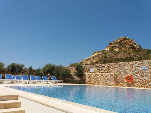 einem Pool mit Stühlen und einem Berg im Hintergrund in der Unterkunft Dreams of Holiday. Apartment with Pool in Marsalforn