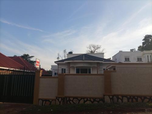 a white house with a blue roof behind a fence at Pearl Furnished Rooms Buloba in Kampala