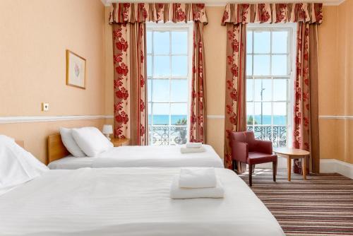 two beds in a hotel room with two windows at Russell Hotel in Weymouth