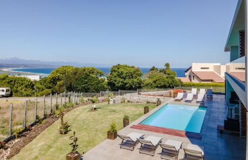 a swimming pool with chairs and the ocean in the background at Hilltop Bayview Luxury Apartments in Plettenberg Bay