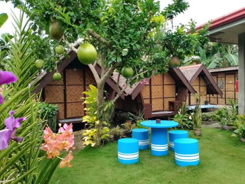 a garden in front of a house with a tree and blue stools at LHOYJEAN Garden Hostel in Batuan