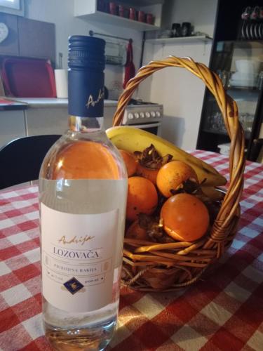 a bottle of wine sitting next to a basket of fruit at Blossom Cottage - Sustainable Tourism Retreat in Laktaši