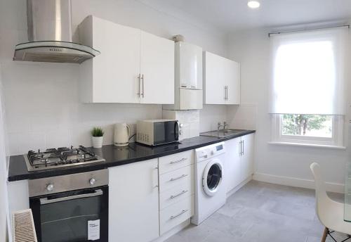 a kitchen with white cabinets and a washer and dryer at London. Gorgeous 2 bed flat near Olympic Park. in London