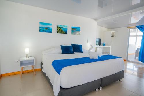 a white bedroom with a large bed with blue pillows at Hotel El Pirata Morgan in Providencia