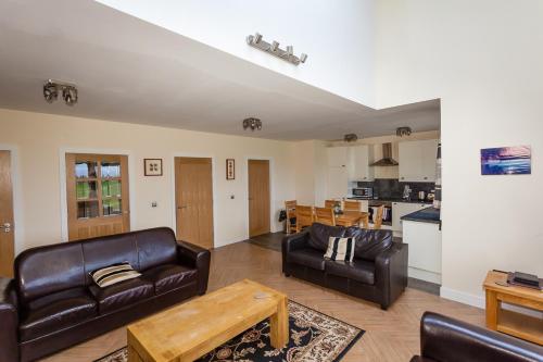 a living room with leather furniture and a kitchen at 2 Eden at Williamscraig Holiday Cottages in Linlithgow