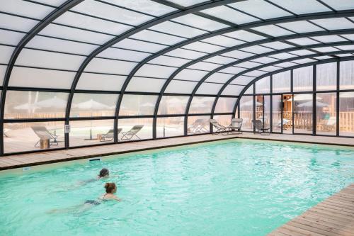 two people swimming in a pool in a building at Huttopia Forêt des Vosges in Barbey-Séroux