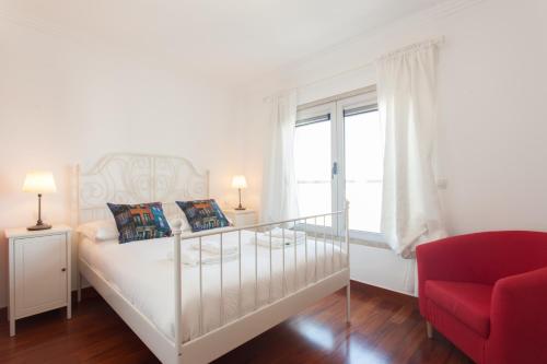 a white bedroom with a bed and a red chair at FLH Expo Cozy Apartment in Lisbon