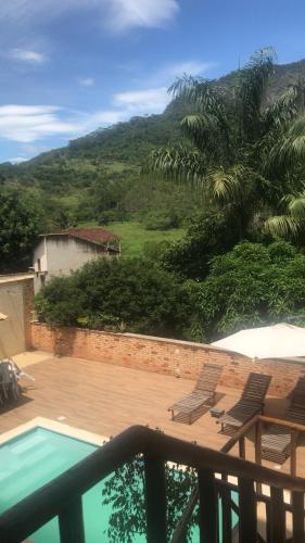 a deck with chairs and a swimming pool with a mountain at Pousada Casa do Jova em Raposo RJ 
