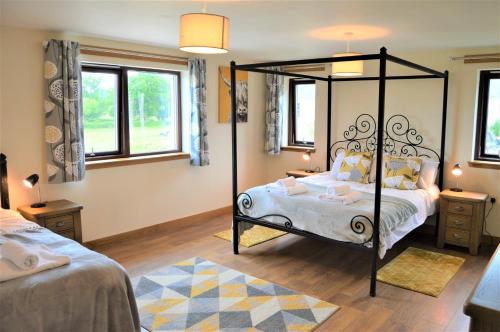 a bedroom with a four poster bed and two windows at The Farmhouse at Williamscraig Holiday Cottages in Linlithgow