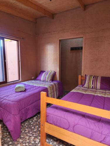 two beds in a room with purple sheets at Las Casas Hostel Atacama in San Pedro de Atacama