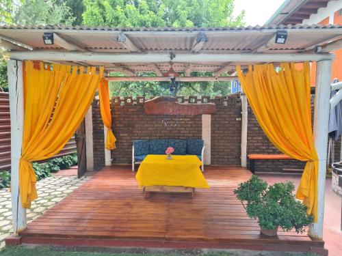 a pergola with yellow curtains and a table on a wooden deck at Alojamiento Quincho Pascual in Las Compuertas