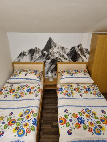 two beds in a room with a mountain mural on the wall at Chata Chopok in Tale
