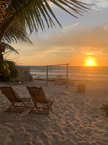 a beach with two chairs and a swing at sunset at Casa Kayab in Puerto Morelos