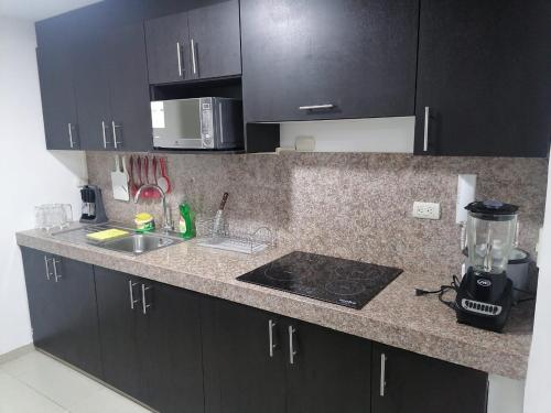 cocina con armarios negros y encimera en Cómodo dpto full equipo 2 hab, seguridad y parqueo privado, en Guayaquil