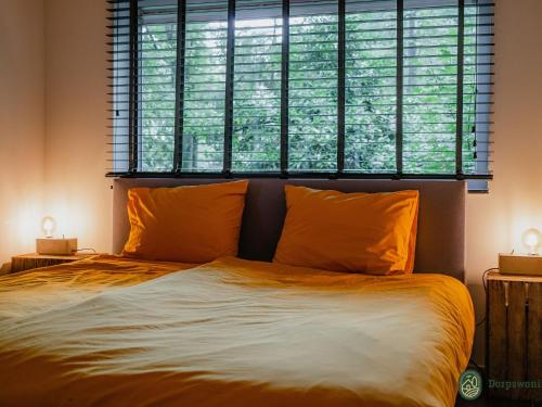 a bed with orange pillows in front of a window at Charming 4-person holiday home on the edge of Leenderstrijp in the forest in Leende