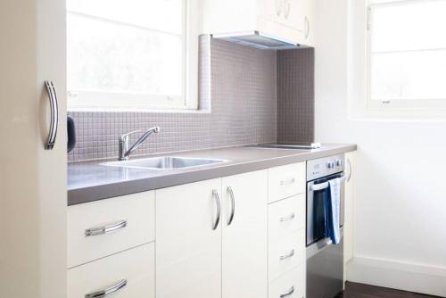 uma cozinha com armários brancos e um lavatório em Joli Light Filled Delight Close to the MCG em Melbourne