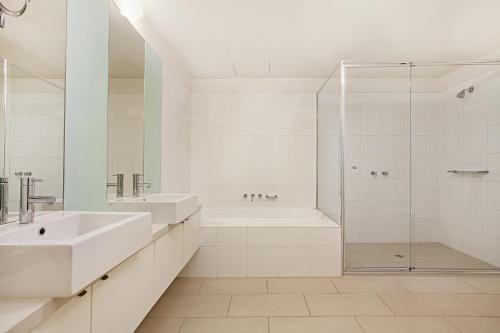 a white bathroom with two sinks and a shower at Melbourne Holiday Apartments Flinders Wharf in Melbourne