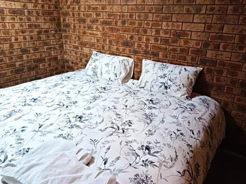 a bed with a white comforter with a brick wall at Western Plains Tourist Park - Dubbo in Dubbo