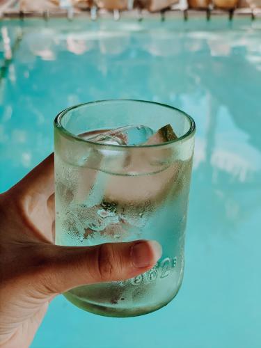 a hand holding a glass of water next to a swimming pool at The Makokola Retreat in Mponda