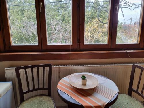 a table and two chairs in a room with two windows at Apartman Poirot in Érd