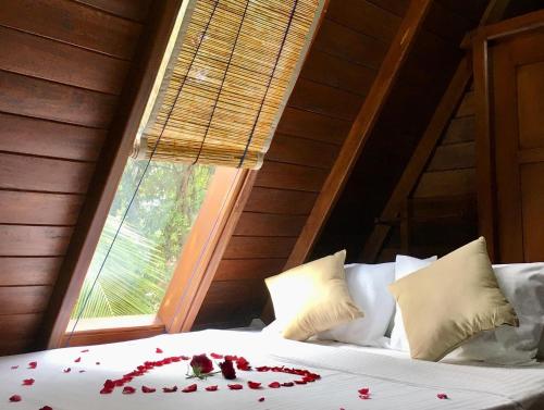 ein Bett mit roten Rosenblättern drauf mit einem Fenster in der Unterkunft Sky View Cabin Unawatuna in Unawatuna