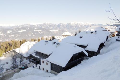 a building covered in snow with mountains in the background at Alpenhäuser Marcius in Sonnenalpe Nassfeld