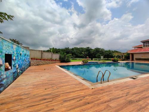 a swimming pool with a wooden deck next to a building at Pushpam Sanskruti Resort Karjat- Pure Veg in Karjat
