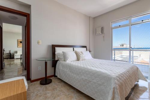 a white bedroom with a bed and a large window at Cobertura de alto padrão com vista para a Praia do Forte in Cabo Frio