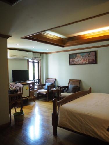 a bedroom with a bed and chairs and a television at Rich Lanna House in Chiang Mai
