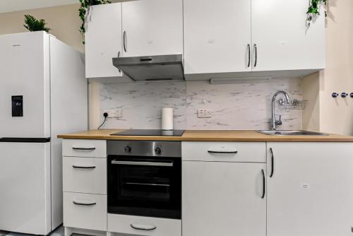 a kitchen with white cabinets and a sink and a refrigerator at Near Canada Water, 2 Beds, Families, Overground in London