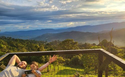 a man and a woman laying on a balcony with their hands in the air at Refugio Mirador del Ocaso in Zipacón