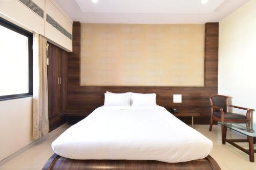 a bedroom with a large white bed and a chair at Hotel Sai Sparsh in Shirdi