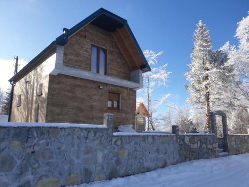 una casa en la nieve con una pared de piedra en Konak Mara- Komovi, en Andrijevica