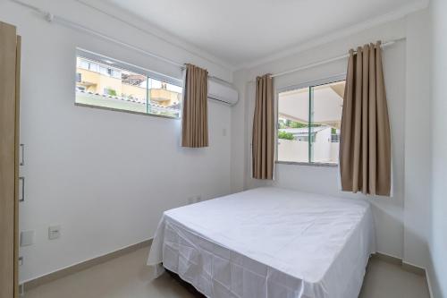 een witte slaapkamer met een bed en 2 ramen bij Apto Pertinho da Avenida da Praia de Bombas - 2 dorms 4 pessoas in Bombinhas