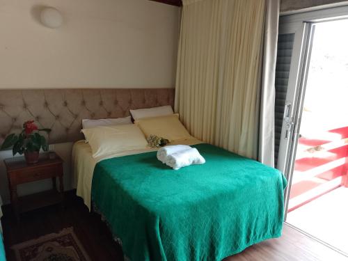 ein Schlafzimmer mit einem Bett mit einer grünen Decke in der Unterkunft Hospedagem Virginia Bracelli in Campos do Jordão